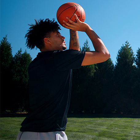 Male model in a black top and gray shorts shooting a basketball. 